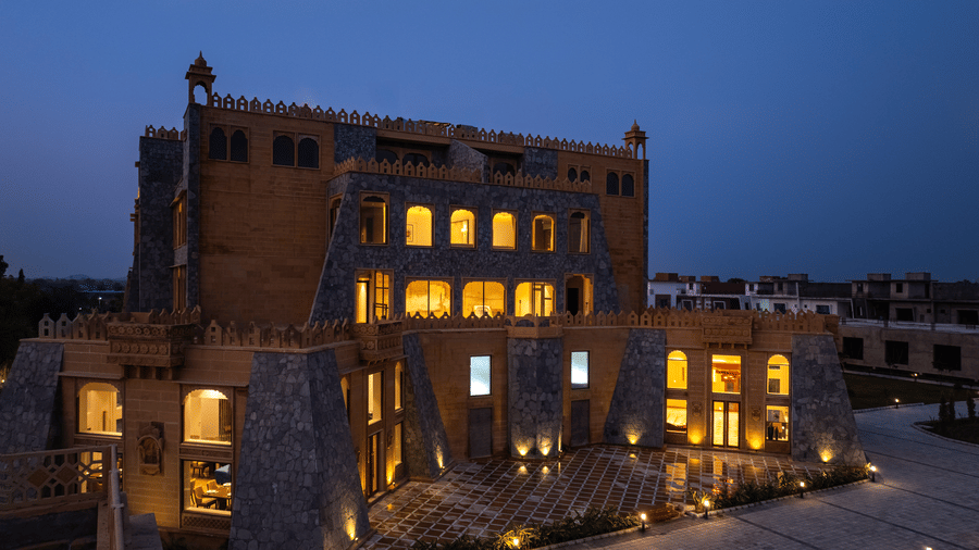 Close-up of the multi-storey stone architecture of EsthereaRaj Leela, Ranakpur, with glowing windows against a deep blue twilight sky.