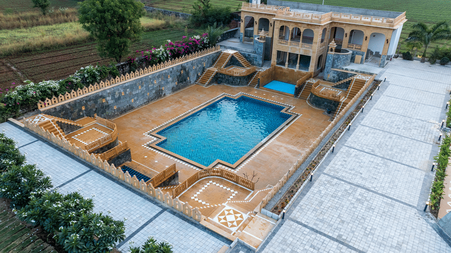 The swimming pool at EsthereaRaj Leela, Ranakpur, featuring a paved patio area and surrounding greenery.