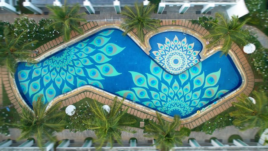 An aerial view of a swimming pool with an intricate blue and white patterned bottom, surrounded by lush greenery | Grand Bay Resort and Spa
