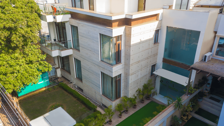 Aerial view showing the stone-clad building with balconies, a green standby generator, a lawn, and potted palms along the path.
