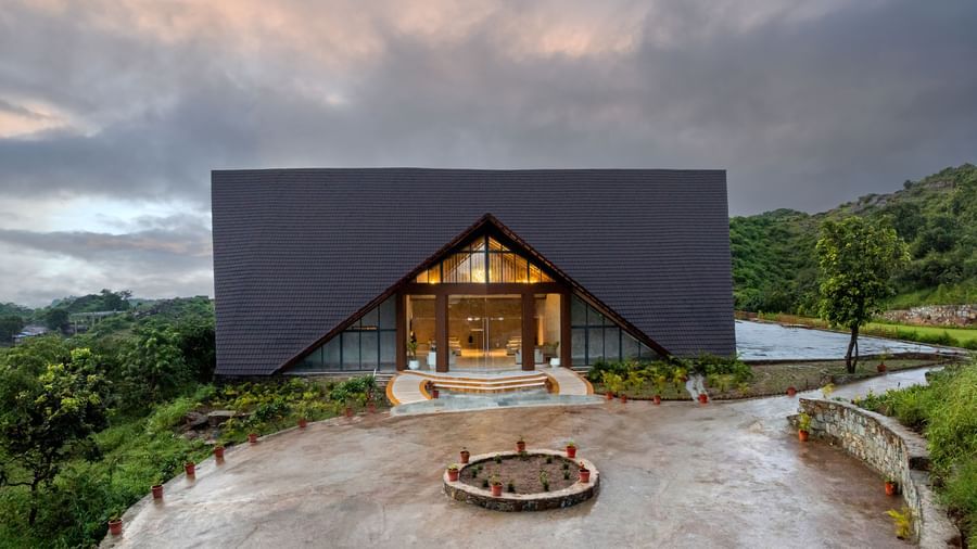 A wide shot of the facade of Osian Valley Resort & Spa, with a large, A-frame entrance and a roundabout with a fire pit in front.