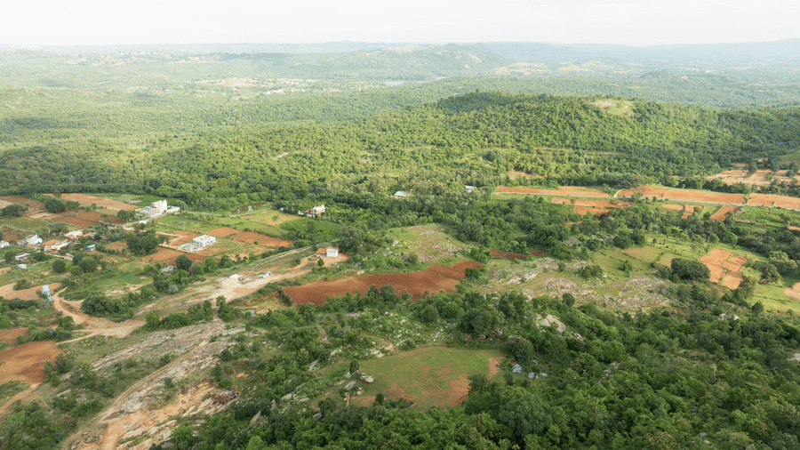 An aerial view reveals a vast expanse of lush green landscape interspersed with patches of reddish-brown earth | RD's Nature Retreat, Bangalore
