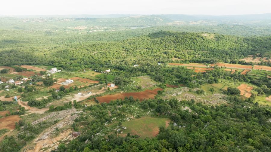 An aerial view reveals a vast expanse of lush green landscape interspersed with patches of reddish-brown earth | RD's Nature Retreat, Bangalore