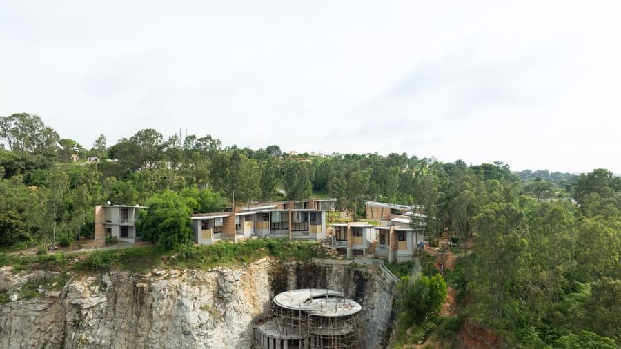 A wide shot of a building complex integrated into a natural, hilly landscape with a body of water visible | Gaia Studio | RD's Nature Retreat, Bangalore