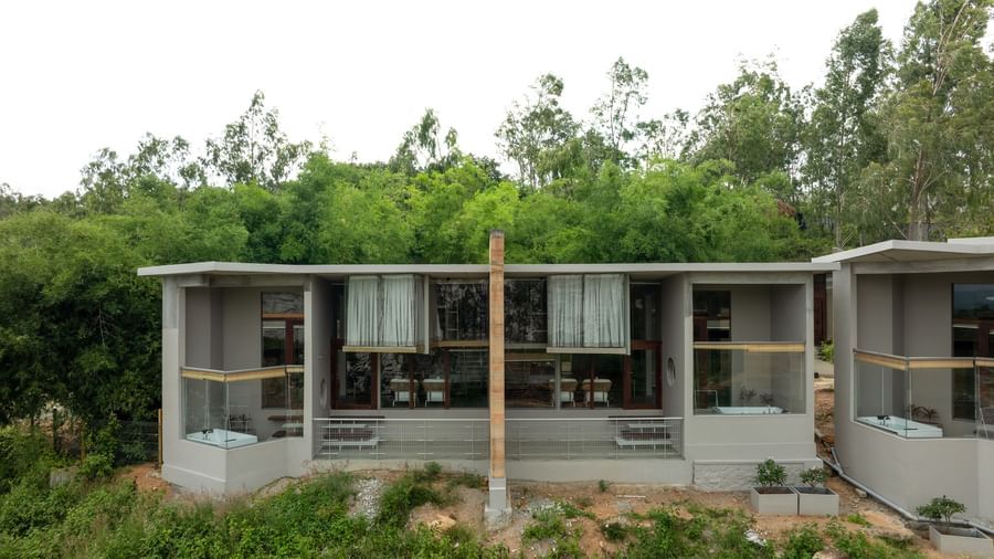 A modern, minimalist building with a flat roof and large windows, surrounded by green foliage under a clear sky | Gaia Studio | RD's Nature Retreat, Bangalore
