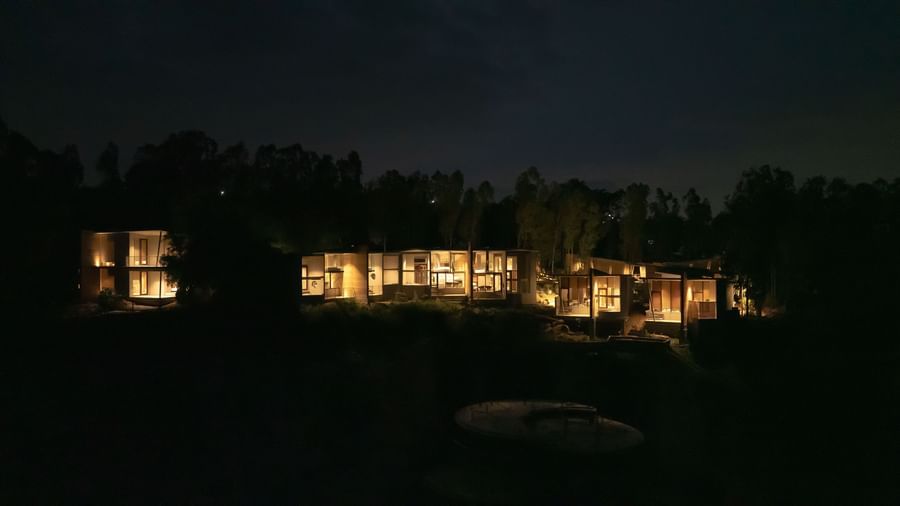 A cluster of illuminated buildings nestled among trees at night, with lights glowing warmly from within | Gaia Studio | RD's Nature Retreat, Bangalore