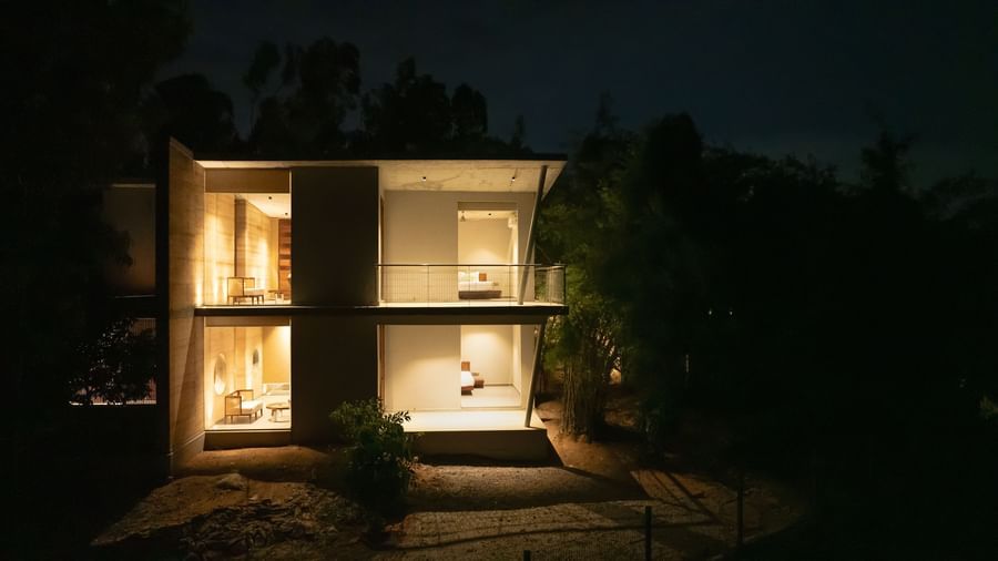A modern house illuminated at night, showcasing its warm interior lighting through large windows | Gaia Studio | RD's Nature Retreat, Bangalore