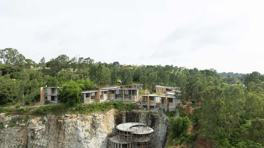 A building complex of Gaia Studio integrated into a natural, hilly landscape with a body of water visible at RD's Nature Retreat, Bangalore