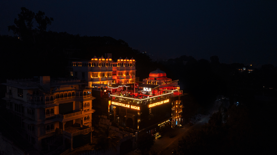 Illuminated hotel complex at night, featuring traditional architecture on a hillside with a dramatic skyline.