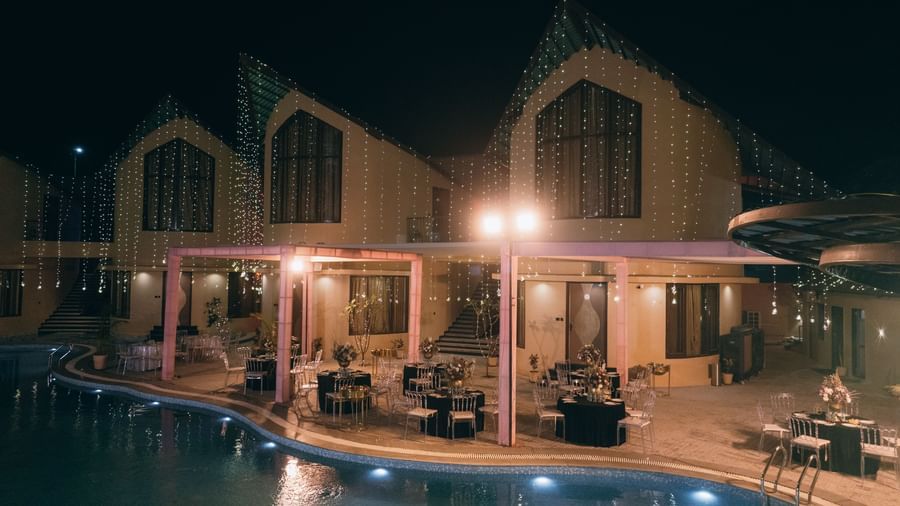 A well-lit building with a pool is visible at night | The Qualia Resort Club & Brewery, Udaipur