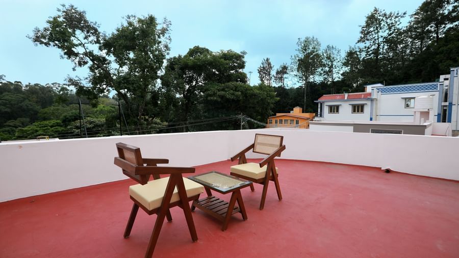 A spacious terrace area at the Terrace cottage with red -coloured flooring, featuring 2 cushioned arm chairs with a coffee table at WOW Naturefull Resorts, Yercaud.