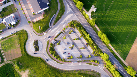 An aerial shot of a roundabout and a road with green grass.