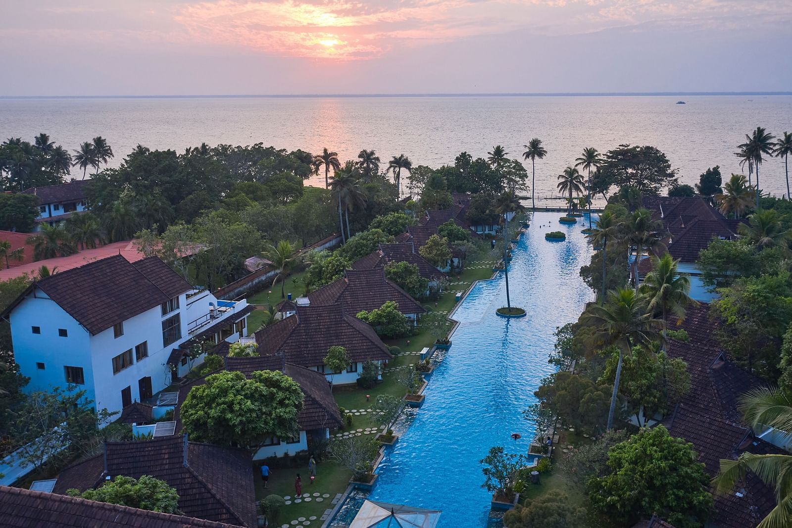 an aerial view of india's largest swimming pool with rooms and trees in view - Rhythm Kumarakom.