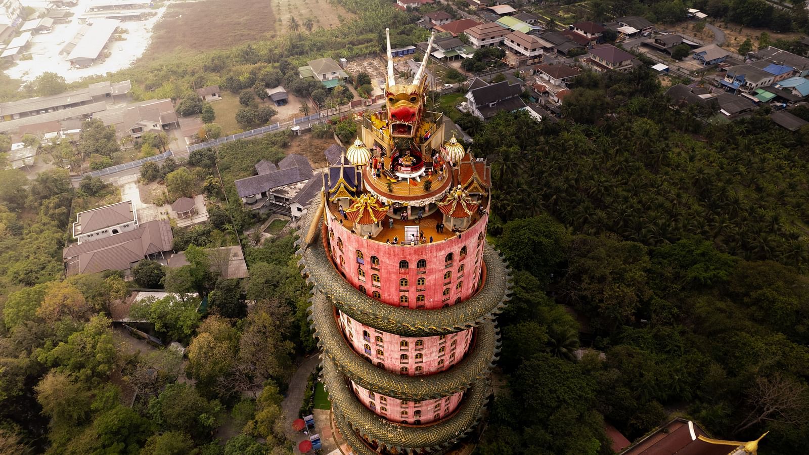 A building in Thailand with a dragon on its roof and trees and other buildings in the background