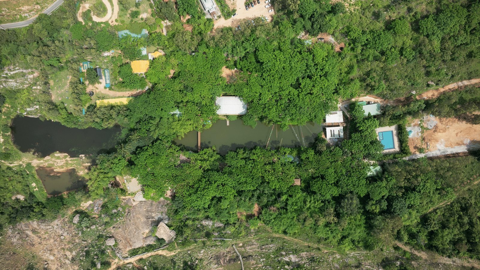 A steep, verdant hillside is dotted with small structures and winding paths, suggesting a terraced or landscaped area at RD's Nature Retreat, Bangalore.