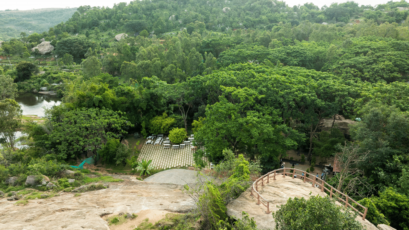 A modern building with a wooden exterior and a pier extends over a calm body of water, bordered by green trees for a perfect Bangalore Weekend Outing | RD's Nature Retreat, Bangalore