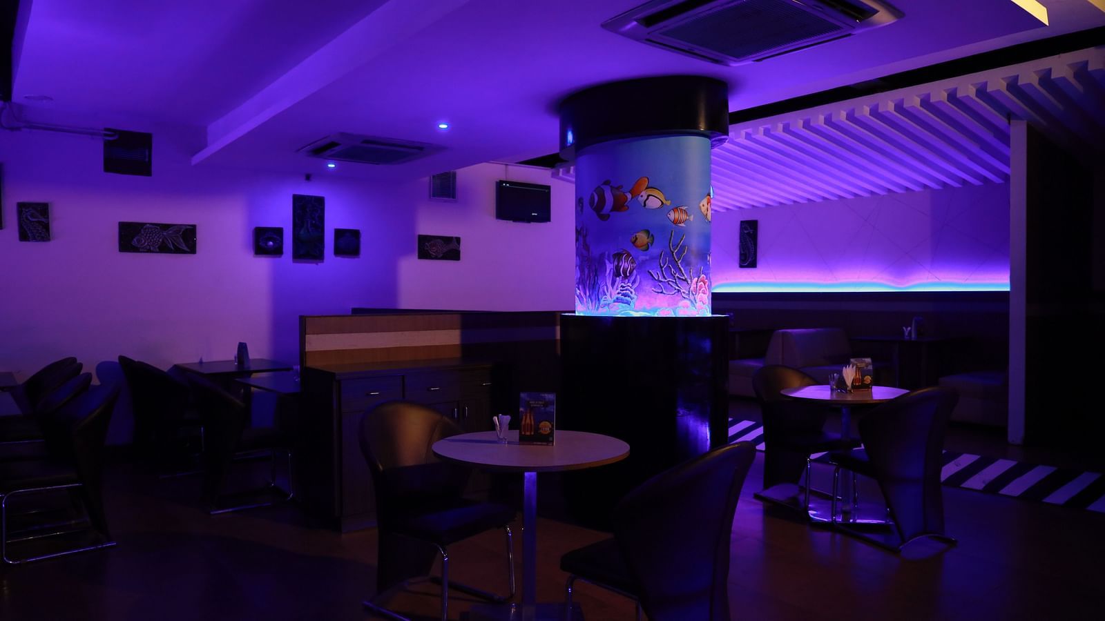 Our bar in Tuticorin, featuring mood lighting, round tables, and a large glass structure representing an aquarium - Regency Tuticorin by GRT Hotels