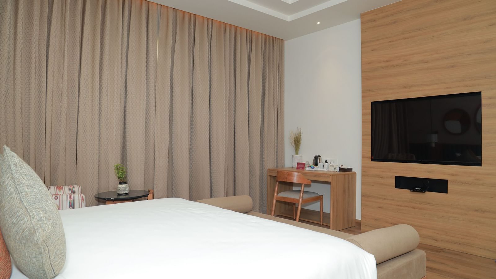 An image of a bed with a pillow placed in front of a wall-mounted television, and a work desk nearby - Regency Tuticorin by GRT Hotels