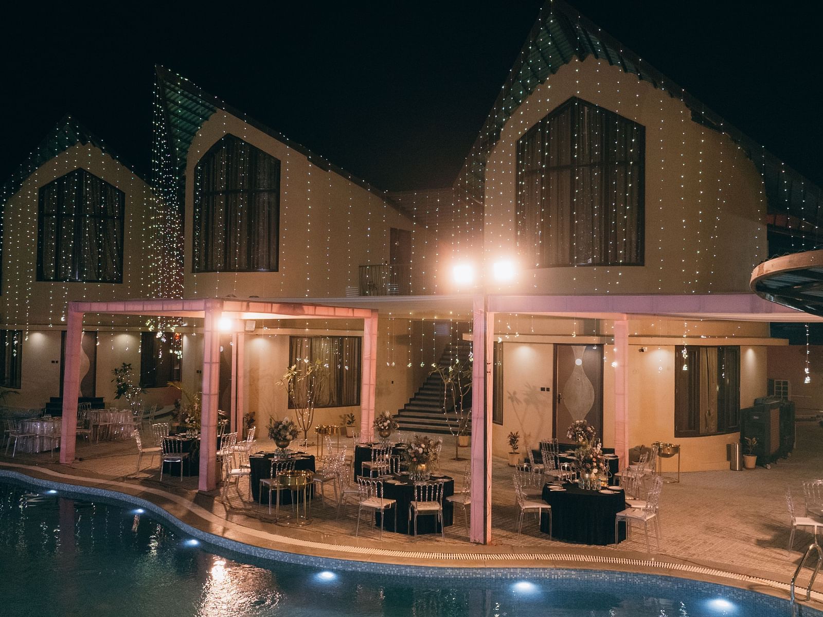 A well-lit building with a pool is visible at night | The Qualia Resort Club & Brewery, Udaipur