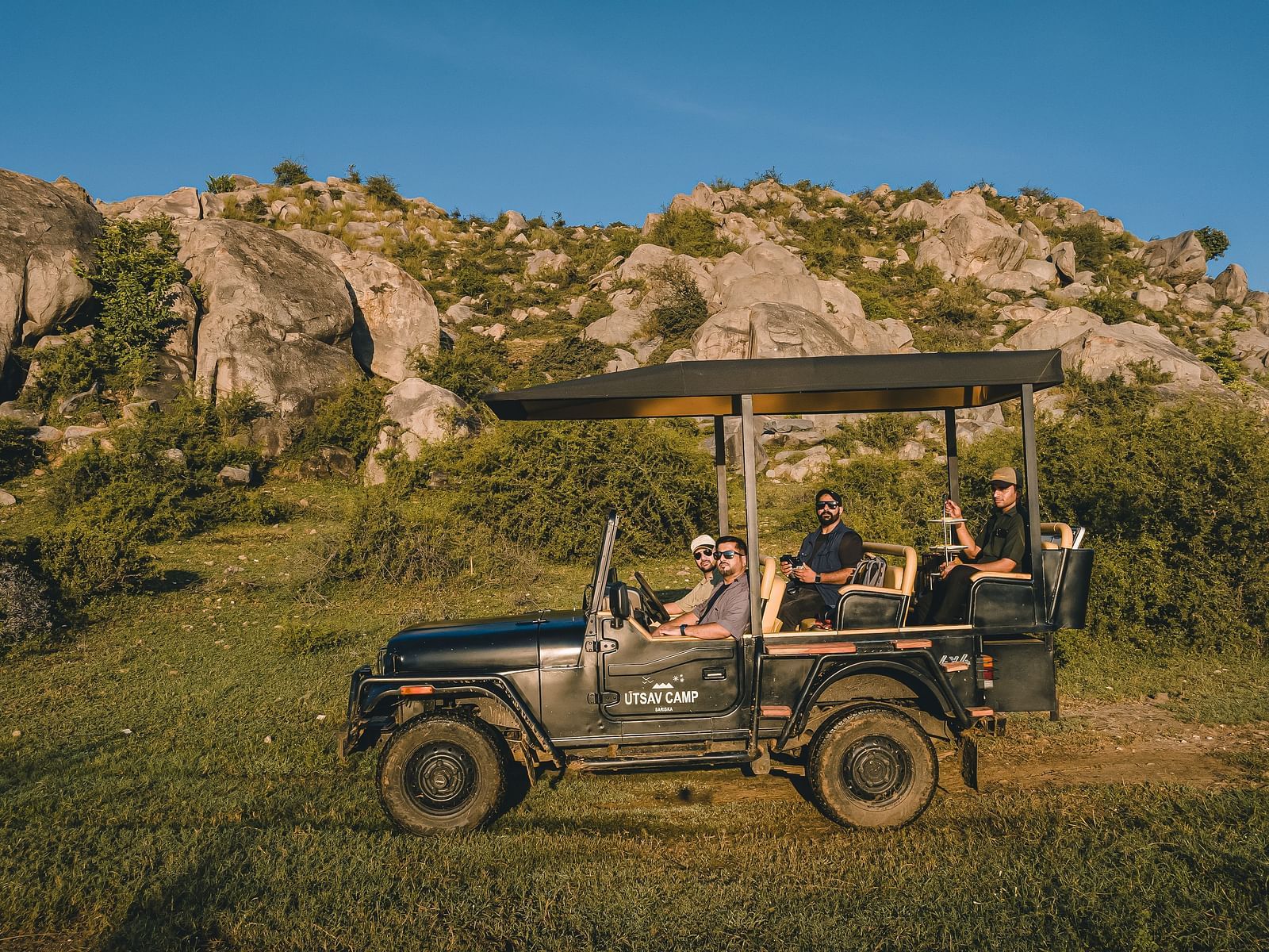 A group of people on a safari jeep with a hill in the background - Utsav Camp Sariska