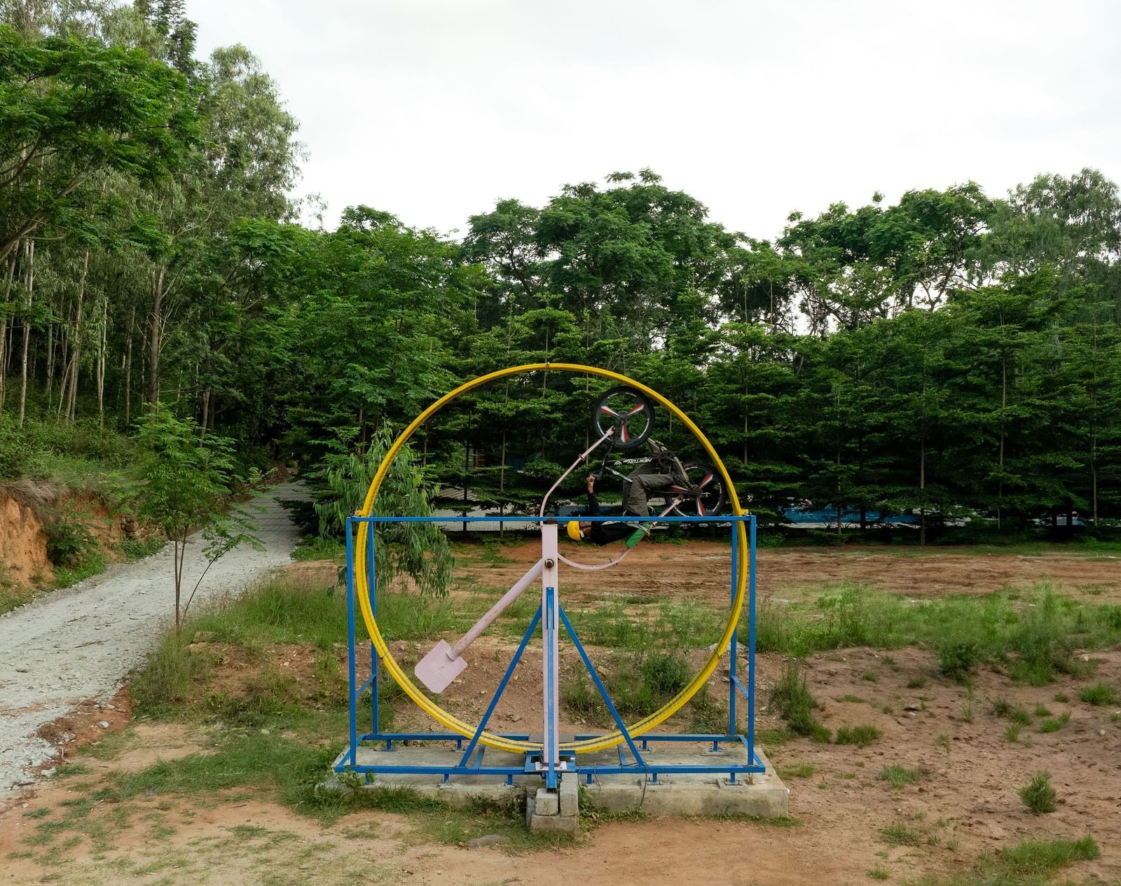 A circular art installation stands in a field with trees in the background under a cloudy sky | RD's Nature Retreat, Bangalore