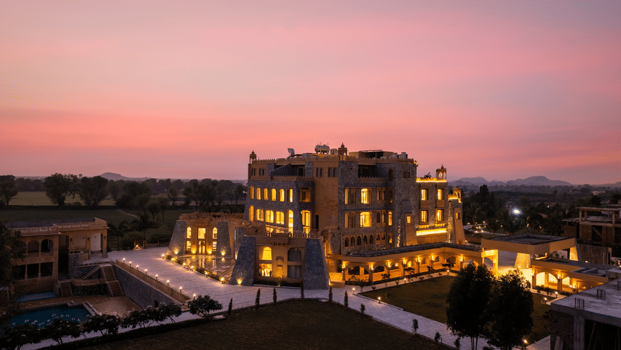 A high angle night view of EsthereaRaj Leela, Ranakpur, featuring yellow lights illuminating the stone facade and paved walkways.