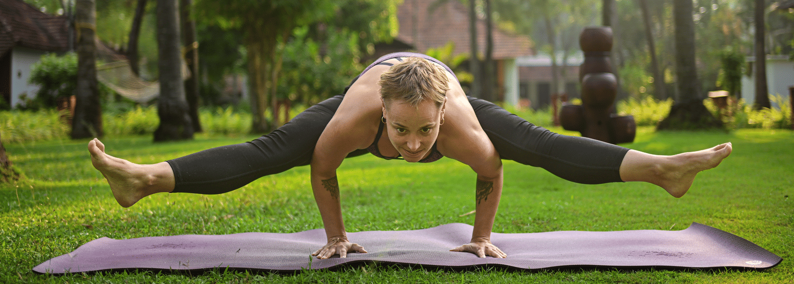 A guest performing an advanced yoga pose on a mat within the lush, palm-fringed gardens of Ayur On The Beach Nattika.