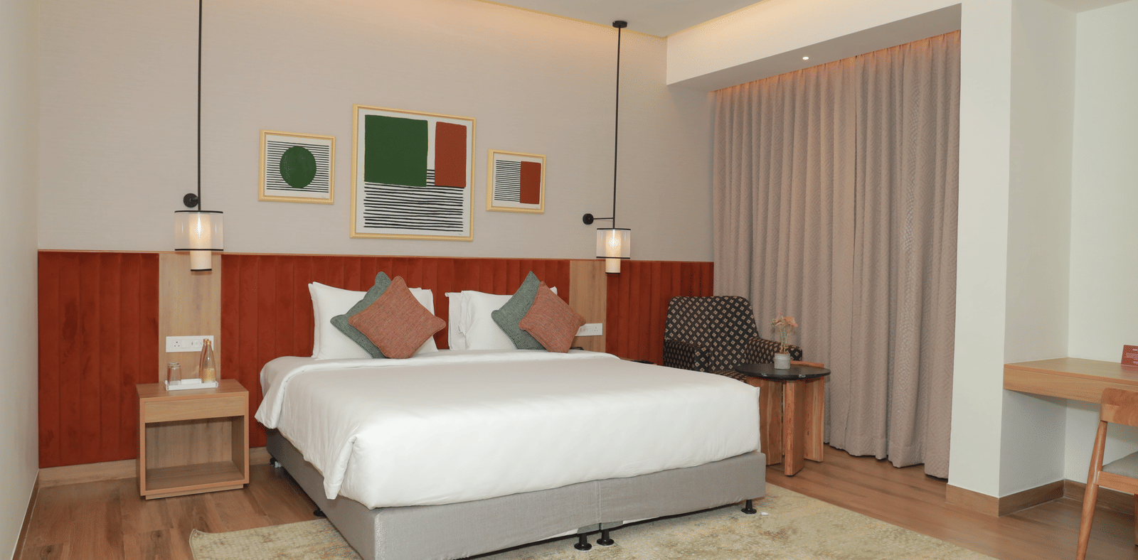 A suite with a large bed, a bed bench, and an upholstered chair in one of our hotel rooms in Tuticorin - Regency Tuticorin by GRT Hotels