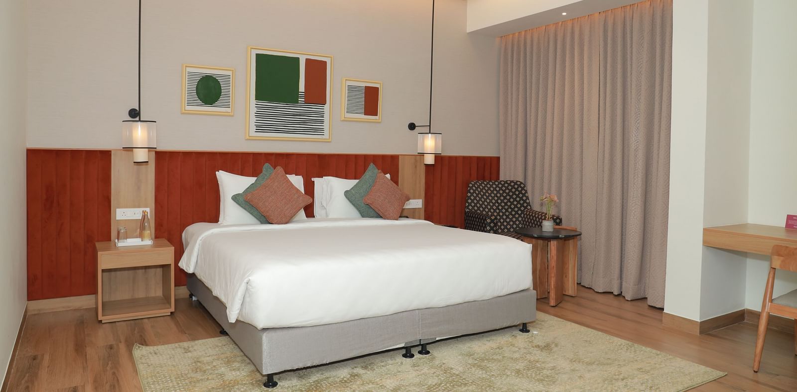 A suite with a large bed, a bed bench, and an upholstered chair in one of our hotel rooms in Tuticorin - Regency Tuticorin by GRT Hotels