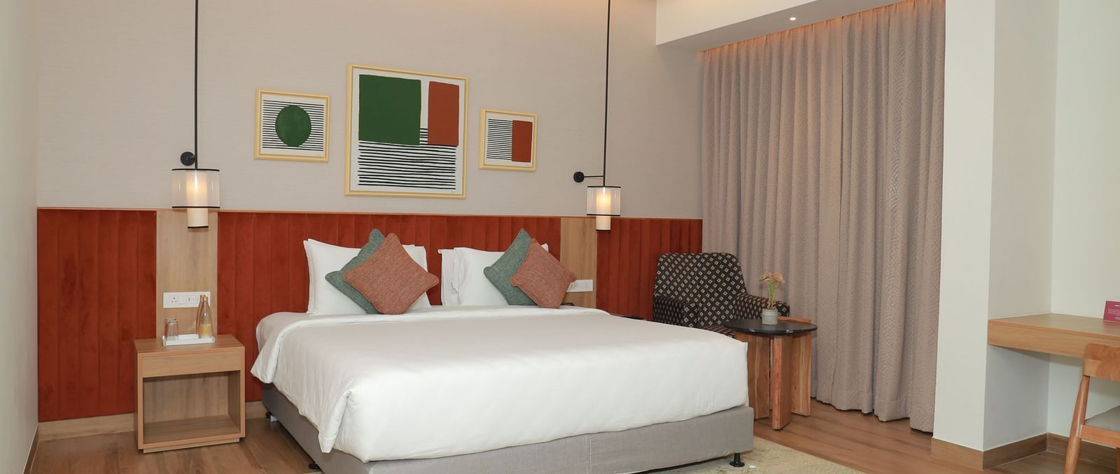 A suite with a large bed, a bed bench, and an upholstered chair in one of our hotel rooms in Tuticorin - Regency Tuticorin by GRT Hotels