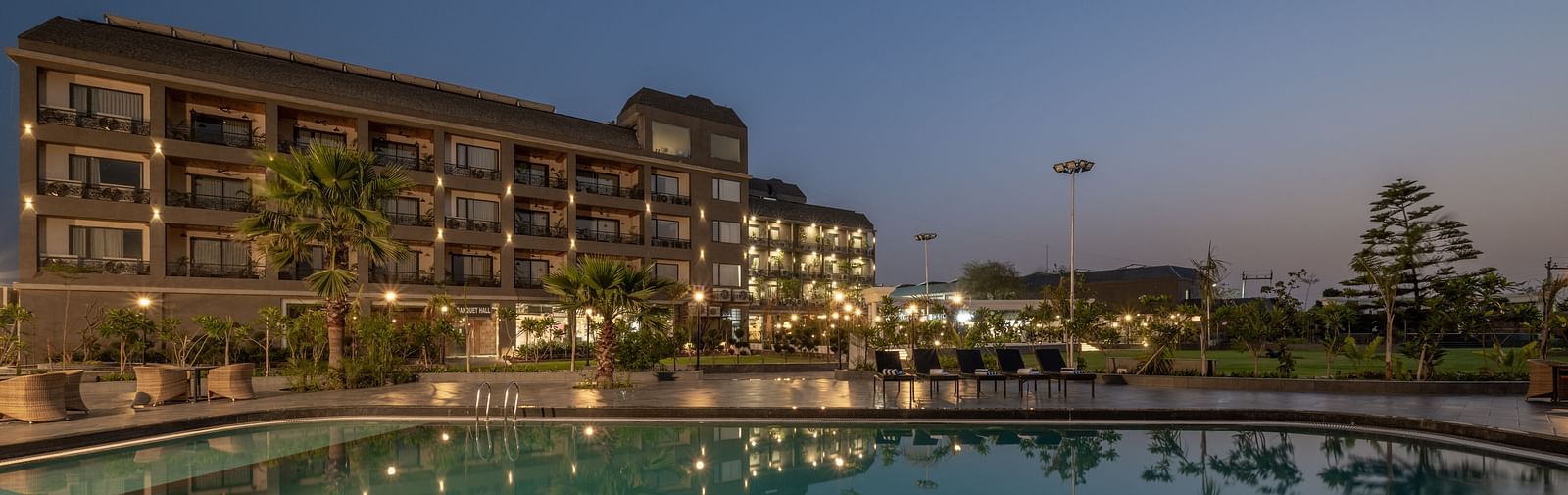 Swimming pool and hotel building at Hotel Highway King, Bagru, with poolside lighting and landscaped garden in the evening.