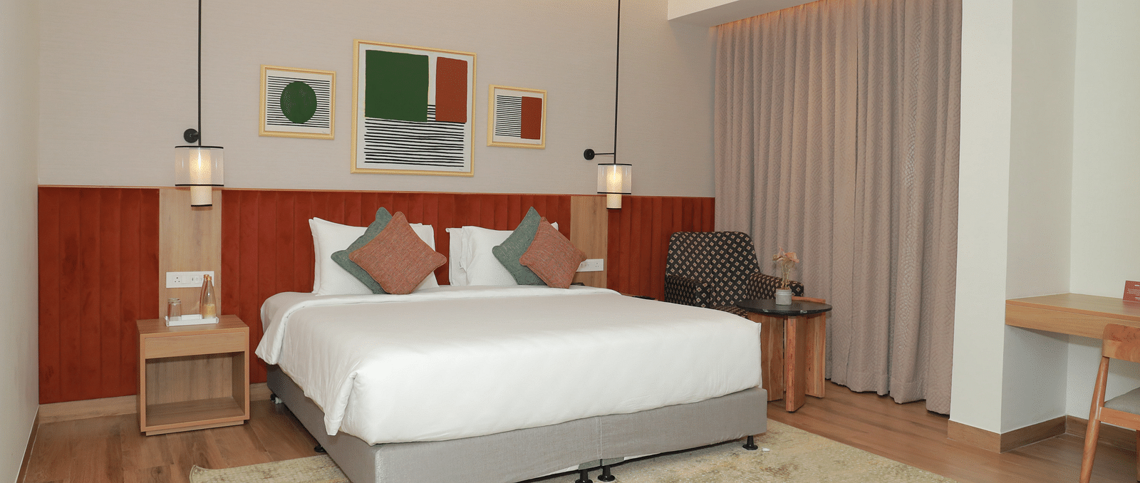 A suite with a large bed, a bed bench, and an upholstered chair in one of our hotel rooms in Tuticorin - Regency Tuticorin by GRT Hotels