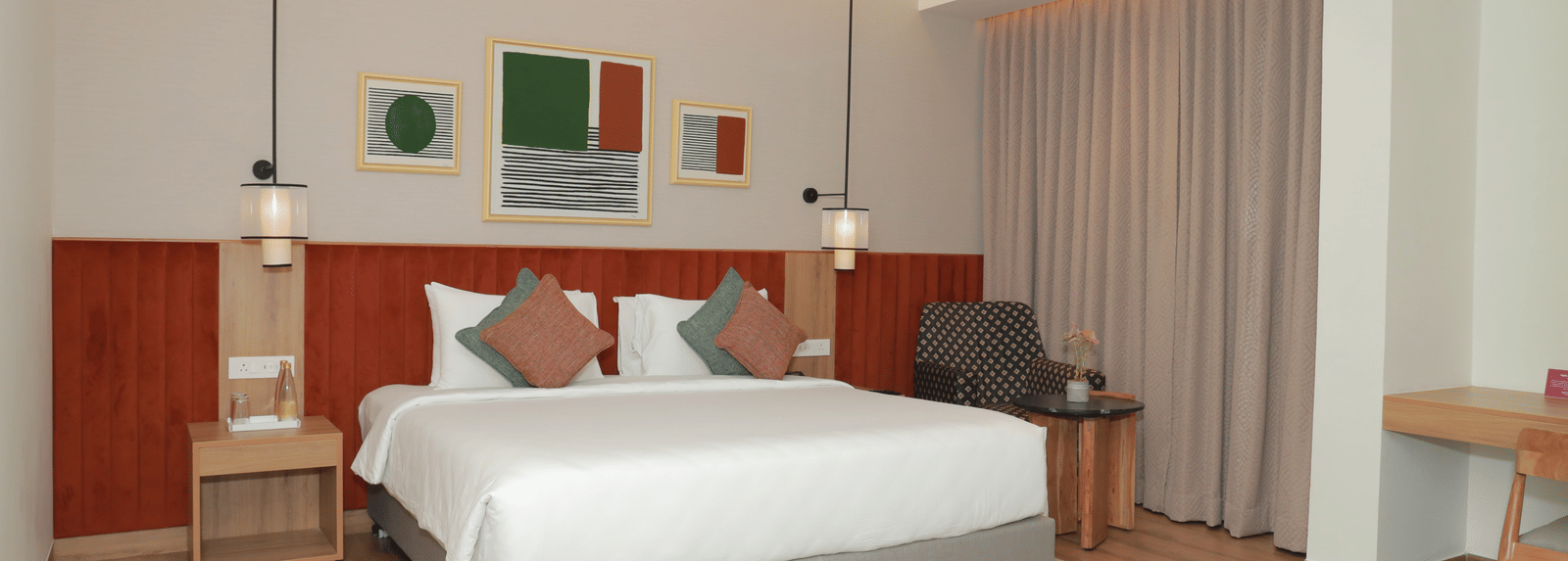 A suite with a large bed, a bed bench, and an upholstered chair in one of our hotel rooms in Tuticorin - Regency Tuticorin by GRT Hotels