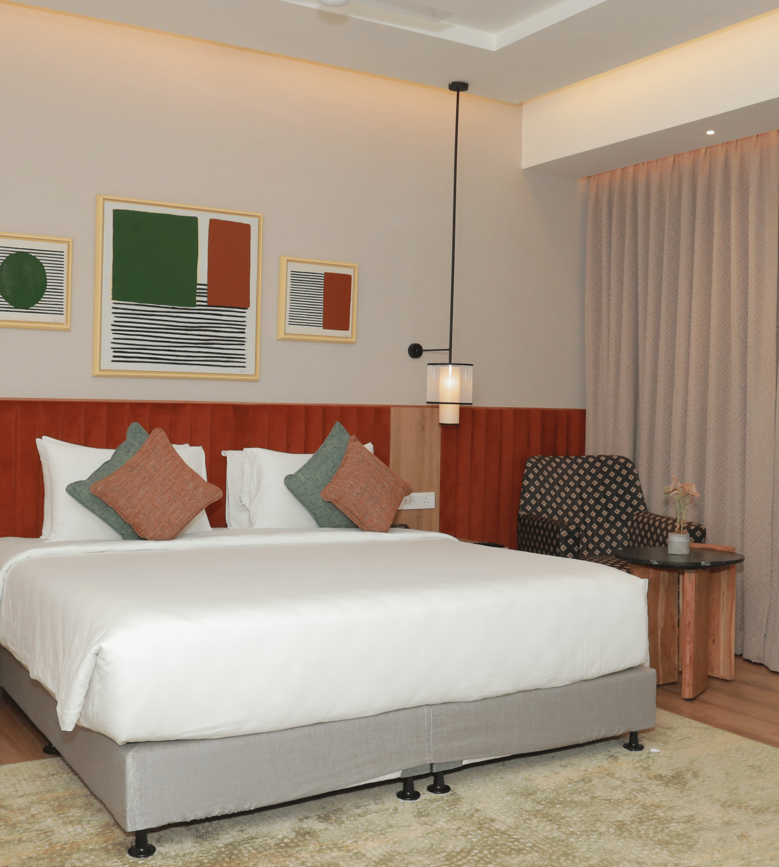 A suite with a large bed, a bed bench, and an upholstered chair in one of our hotel rooms in Tuticorin - Regency Tuticorin by GRT Hotels