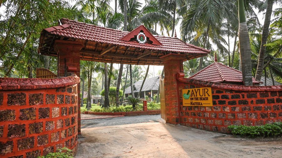 The ornate entrance gate of Ayur On The Beach Nattika topped with a traditional tiled roof and surrounded by greenery.