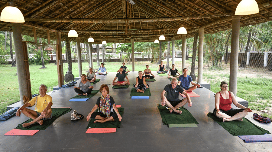 A group of guests participating in a guided yoga session inside a large open-air thatched pavilion at Ayur On The Beach Nattika.