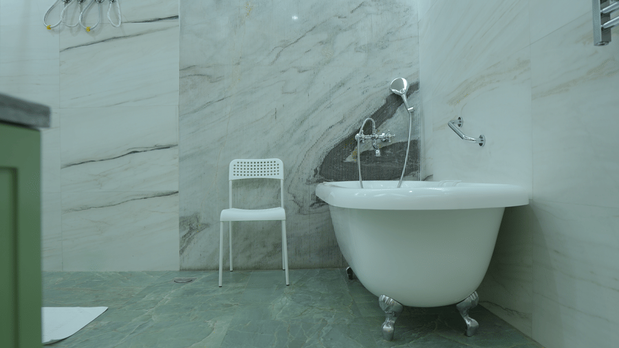 A bathroom at The Heritage Club Tripura Castle Hotel and Spa, Shillong featuring a freestanding bathtub, a chair, marble walls, and a hand shower.