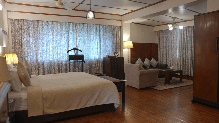 A bedroom at The Heritage Club Tripura Castle Hotel and Spa, Shillong featuring a king size bed, a seating area with sofas, a coffee table, curtains, and a wardrobe.