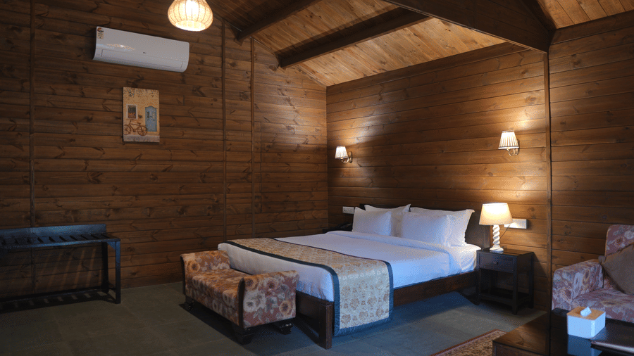 A bedroom at The Heritage Club Tripura Castle Hotel and Spa, Shillong featuring a double bed, a bench, a luggage rack, an air conditioner, and wood panelled walls.  