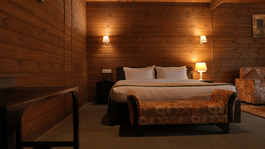 A bedroom at The Heritage Club Tripura Castle Hotel and Spa, Shillong featuring a double bed, a upholstered bench, bedside lamps, and wood panelled walls.  