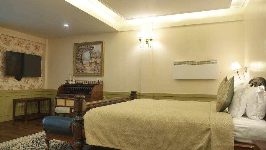 A bedroom at The Heritage Club Tripura Castle Hotel and Spa, Shillong featuring a king size bed, a roll-top writing desk, a television, and wall lights.  