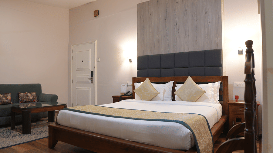 A bedroom at The Heritage Club Tripura Castle Hotel and Spa, Shillong featuring a king size bed, a sofa set, a coffee table, and bedside lamps.  