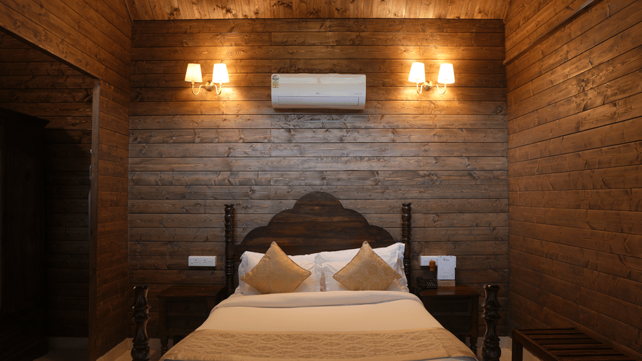 A bedroom at The Heritage Club Tripura Castle Hotel and Spa, Shillong featuring a double bed, bedside tables, wall lamps, wood-panelled walls, and an air conditioner.  