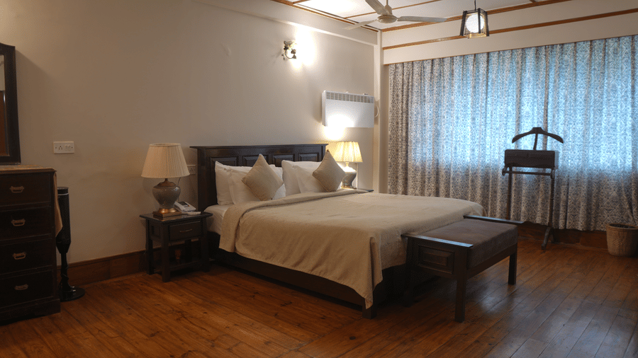 A bedroom at The Heritage Club Tripura Castle Hotel and Spa, Shillong featuring a king size bed, bedside tables, lamps, a bench, and a clothes stand.
