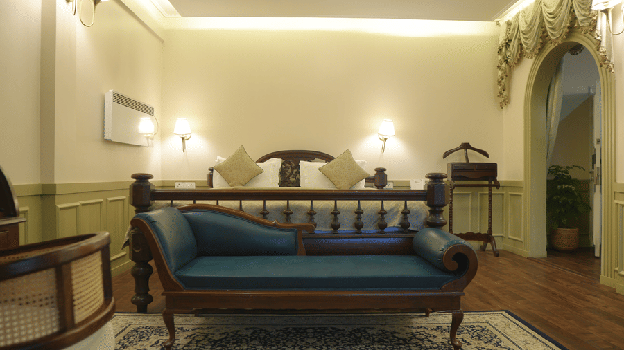 A bedroom at The Heritage Club Tripura Castle Hotel and Spa, Shillong featuring a wooden bed, a blue chaise lounge, wall sconces, and an arched doorway.  