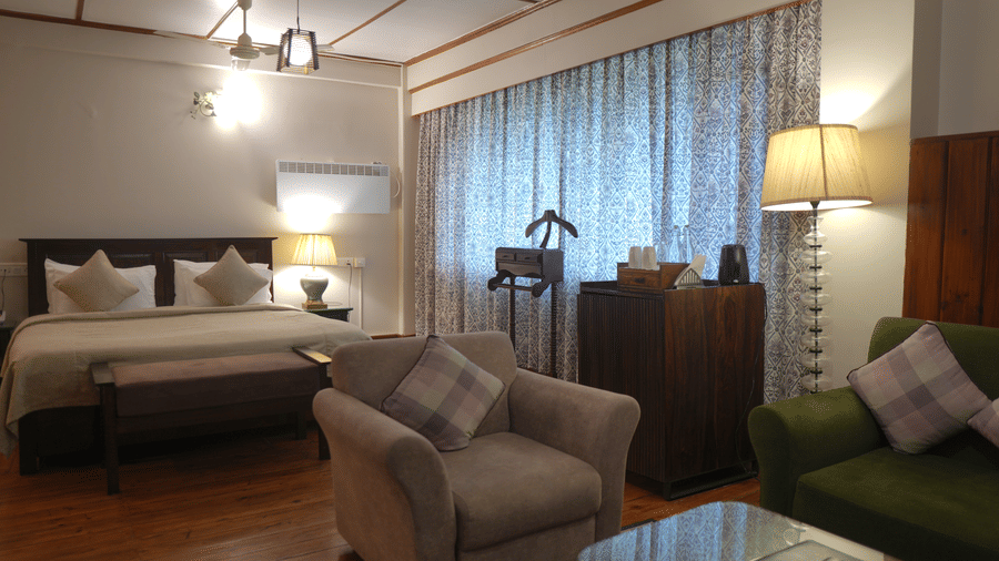 A bedroom at The Heritage Club Tripura Castle Hotel and Spa, Shillong featuring a king size bed, armchairs, a coffee table, lamps, and a clothes stand.
