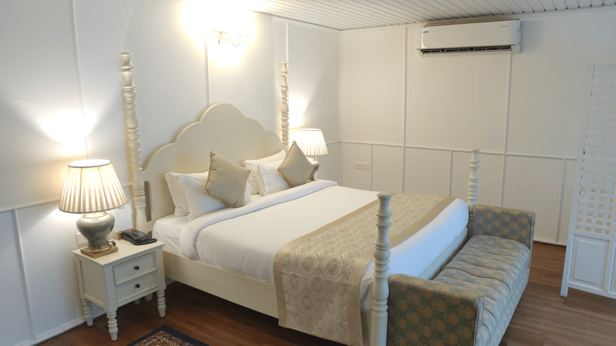 A bedroom at The Heritage Club Tripura Castle Hotel and Spa, Shillong featuring a king size bed, a bench, bedside tables, lamps, and an air conditioner.  