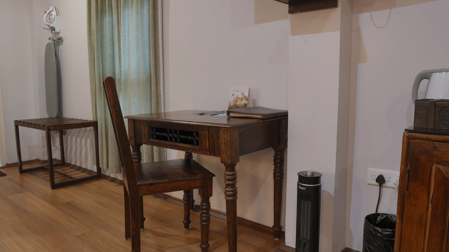 A living area at The Heritage Club Tripura Castle Hotel and Spa, Shillong featuring a wooden writing desk, a chair, an ironing board, and a room heater.  