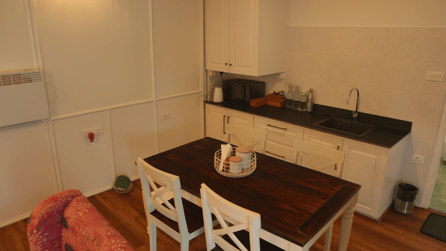 A dining area and kitchenette at The Heritage Club Tripura Castle Hotel and Spa, Shillong featuring a dining table, 2 chairs, cabinets, a sink, and a microwave.