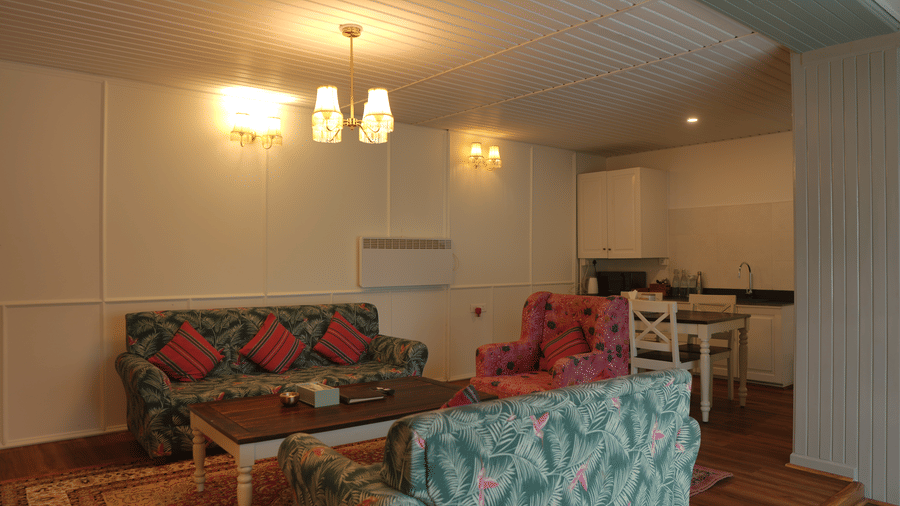A living room and dining area at The Heritage Club Tripura Castle Hotel and Spa, Shillong featuring sofas, a coffee table, a dining set, lights, and a kitchenette.